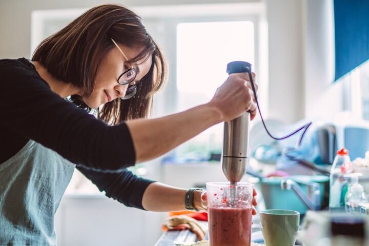 Woman making berry smoothie with stick blender