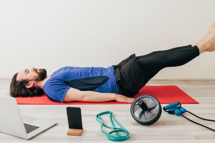 Man performs leg lowers with assorted exercise equipment on the floor around him
