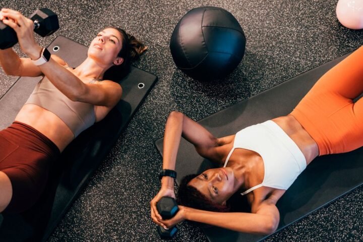 Two women lying on the floor lowering a dumbbell behind their heads